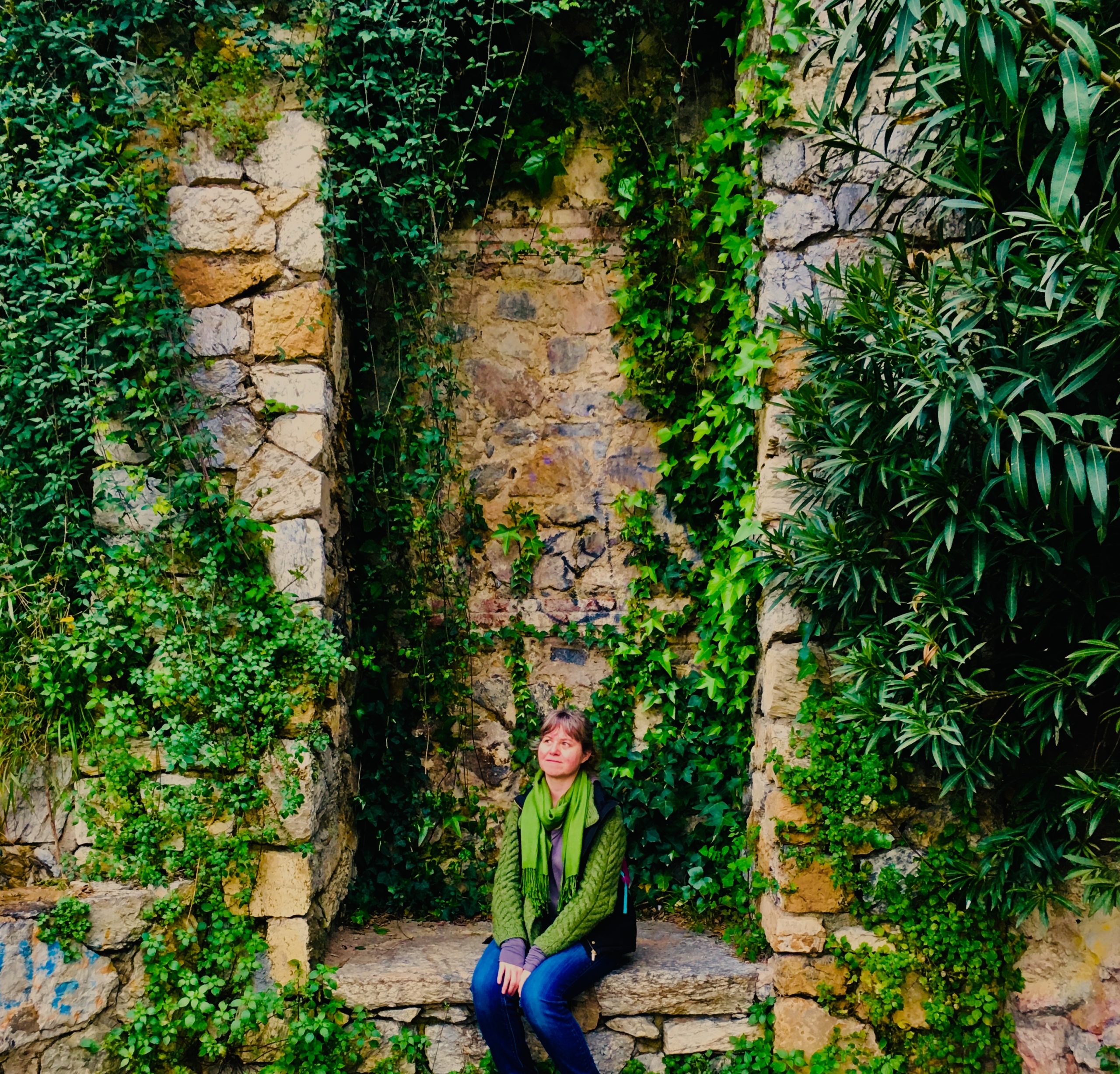 photo of Alicia Champlin sitting in under a vine covered stone wall