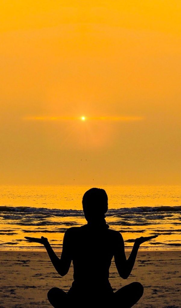 silhouette of a woman sitting on a beach with golden sky